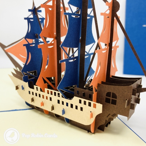 A pop-up galleon with orange and blue sails on a brown hull, beside a blue cover and four blue dolphins.