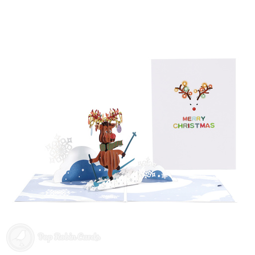 Rudolf the reindeer skiing in a 3D pop-up card, in a striped scarf with lit antlers, on a snowy slope with paper snowflakes