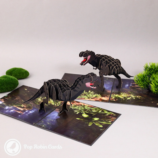 Pop-up T-Rex dinosaur with open jaws and a striped body of layered card, striding across a printed woodland floor of ferns.