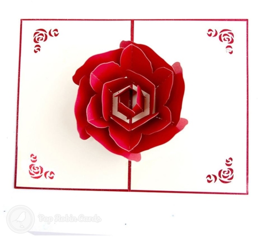 Open card with a layered red paper rose, on cream pages with red edges and small rose cut-outs in each corner.