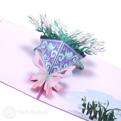 Pop-up bouquet of white flowers in a purple cone with a pink bow, beside printed snowdrops on the right-hand page